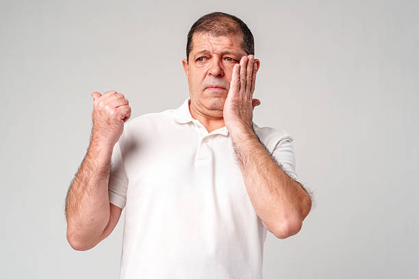 istock An older man holds his cheek, showing concern, against a plain background 2233488203