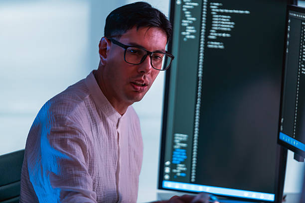 istock Programmer wearing glasses codes at dual monitors in modern office, lit by cool blue light. Scene highlights developer focus, software engineering, technology, and computer workstation setup. 2233491748