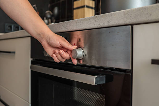 istock Close-up of a woman's hand adjusting a silver control knob on a modern built-in kitchen oven with a digital display showing 2233496806