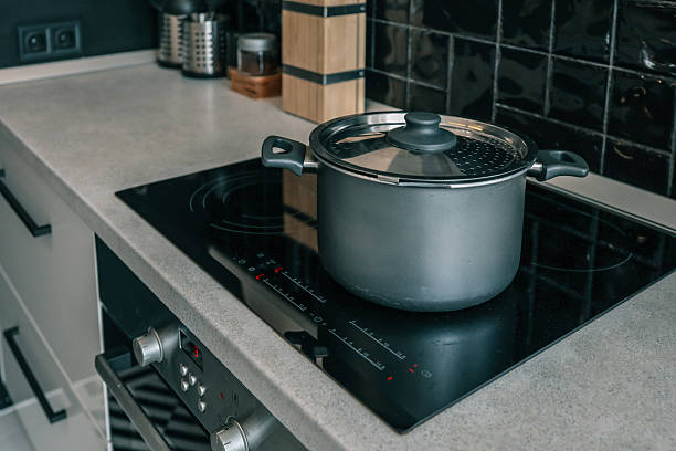istock Modern kitchen interior with a matte black cooking pot on a sleek induction cooktop, surrounded by black tiles, a knife block, and metal utensil holders 2233496807