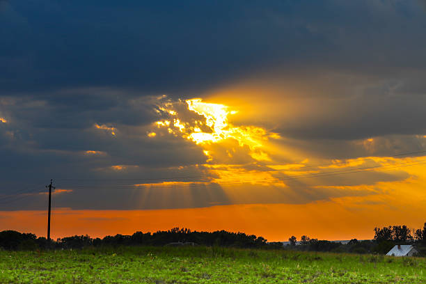 Sunset over a rural field. Sunbeams breaking through dark clouds illuminate the sky with golden light.