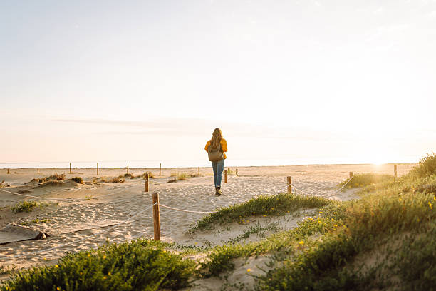 istock A female traveler with a backpack and a bright jacket enjoys a walk on a sandy beach during sunset. 2233499850