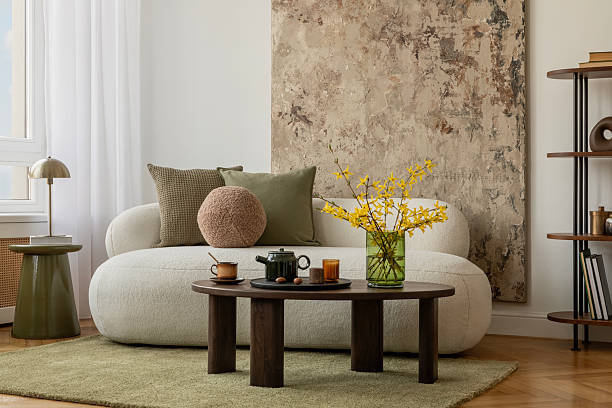 istock Light-filled interior with sculptural decor, minimalist sofa,  decorations and yellow spring flowers in a green glass vase. 2233501481