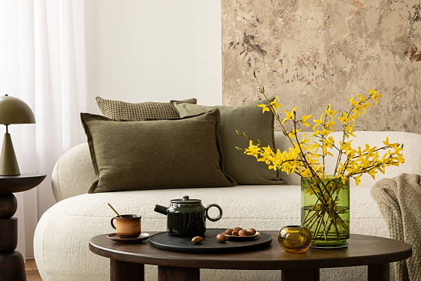 istock Modern sofa with olive pillows, beige blanket, and wooden coffee table decorated with tea set, nuts, and yellow flowers in green vase. 2233501751
