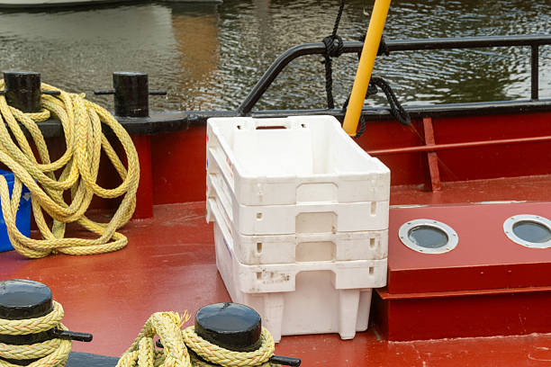 Empty white plastic crates stacked on the deck of a red fishing boat with mooring ropes