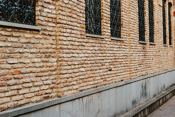 A weathered brick wall features ornate iron bars covering the windows. The sunlight highlights the texture of the bricks, creating a rustic urban ambiance.