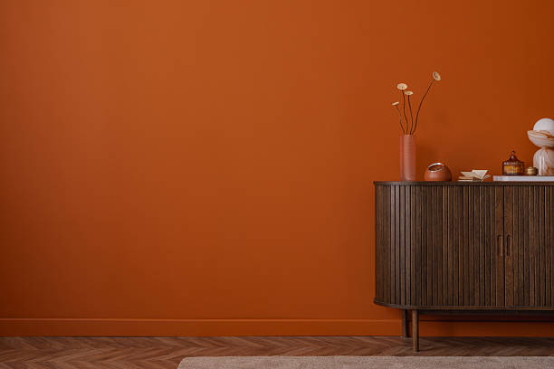 istock Minimalist interior with decorative objects and a pink ribbed vase on a wooden cabinet against a plain burnt orange wall. Calm, modern composition. Copy space. 2233506488