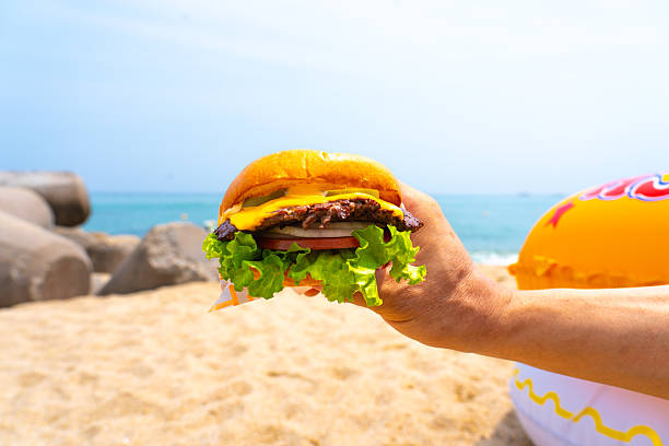 Man holding burger in a hand against beach background