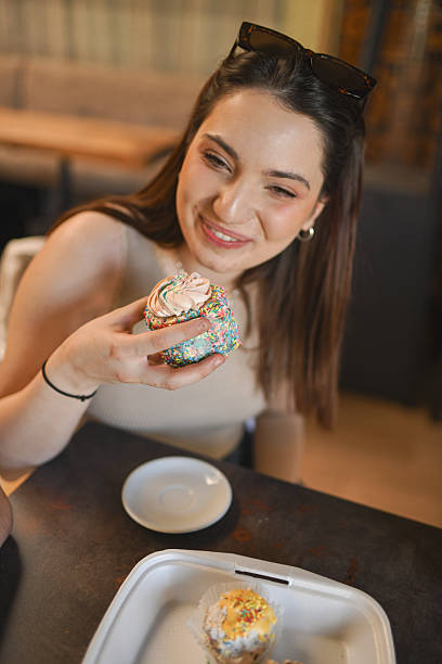 istock Beautiful Woman Smiling While Indulging In Sweet Colorful Cupcake 2233510909