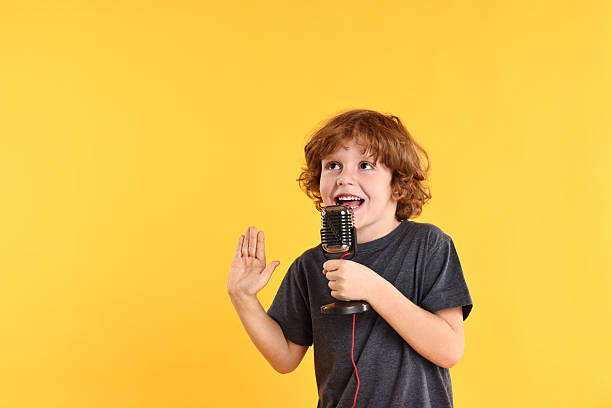 istock Little boy with microphone singing on yellow background 2233511122