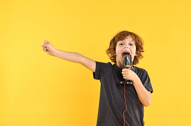 istock Little boy with microphone singing on yellow background 2233511159