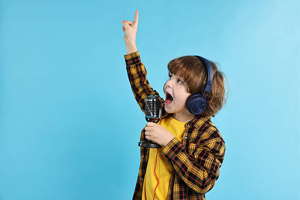 istock Little boy with microphone and headphones singing on light blue background, space for text 2233511210