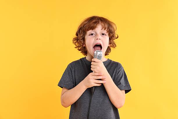 istock Little boy with microphone singing on yellow background 2233511649