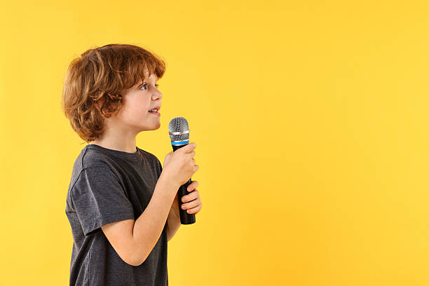 istock Little boy with microphone singing on yellow background, space for text 2233511956