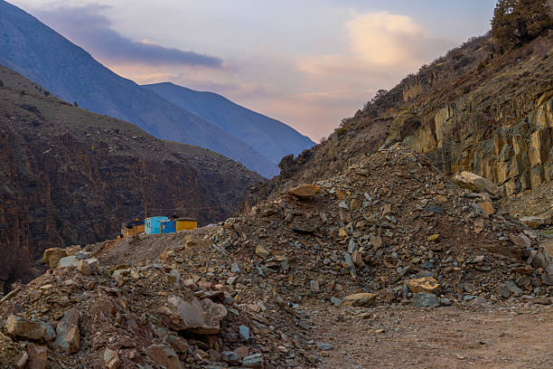 Three distinct buildings stand amidst rocky terrain in a serene mountainous region at dusk. The blue building contrasts with the tan and brown structures, creating a peaceful atmosphere.