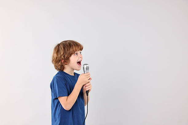 istock Little boy with microphone singing on light grey background, space for text 2233513125