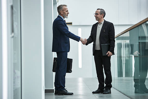 istock Two Middle Aged Caucasian Men Shaking Hands in Modern Office Corridor 2233513892