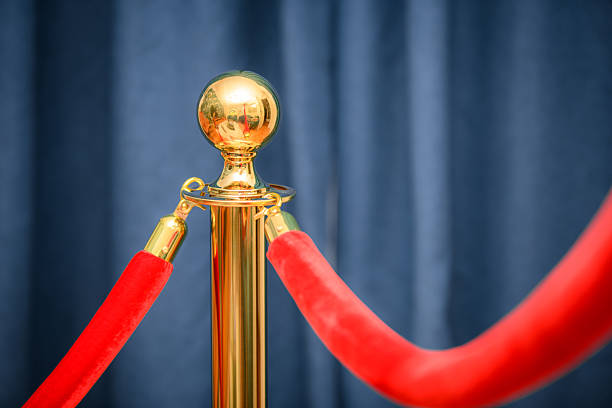 Wide panoramic view rope fencing with gold pillars with a red carpet for celebrities and guests of an expensive event with crowds of people