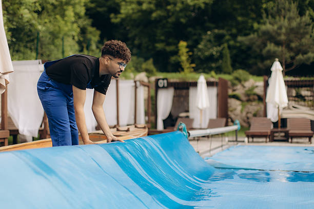 istock Pool maintenance worker unrolling thermal cover at resort hotel 2233527227