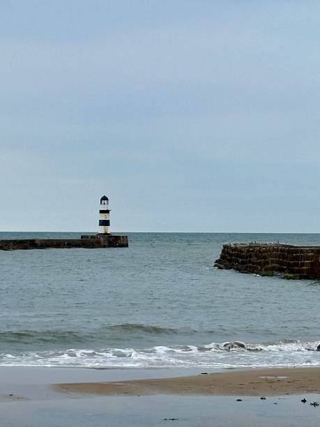 istock A distant lighthouse overlooks the bay, standing tall on the pier with calm waters stretching out. The scene evokes coastal charm, safety, and maritime heritage against a soft sky and sea. 2233532271