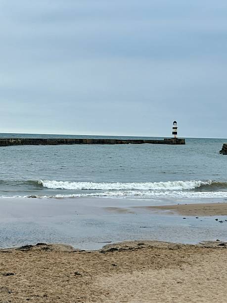 istock A distant lighthouse overlooks the bay, standing tall on the pier with calm waters stretching out. The scene evokes coastal charm, safety, and maritime heritage against a soft sky and sea. 2233532274