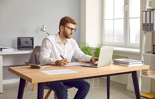 istock Businessman using laptop and making notes on paper in his office 2233536256