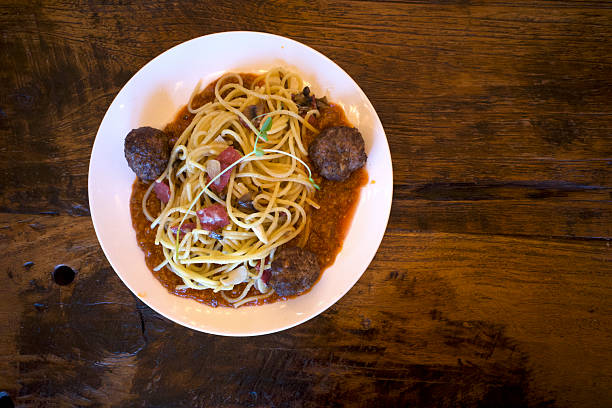 Spaghetti served on a white plate, garnished with a fresh microgreen on an old wooden table.
