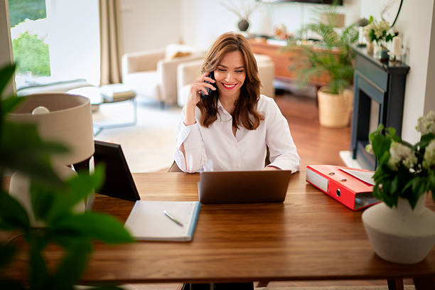 istock Brunette haired businesswoman sitting at home and using cell phone and computer laptop 2233540672