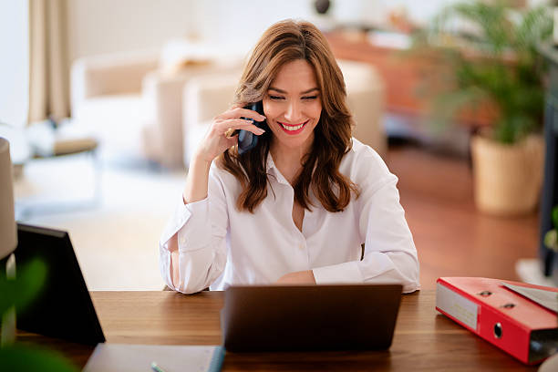 istock Confident woman sitting at desk at home and using a computer notebook and smartphone 2233540678