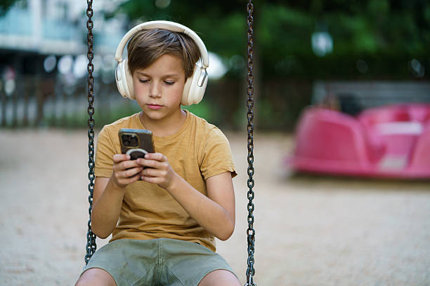 A young boy wearing a vivid pink shirt holds a game controller and looks focused against a solid blue studio backdrop.