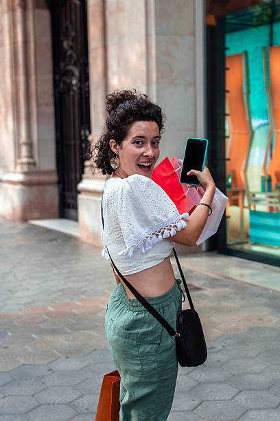 istock Young woman showing mobile phone screen while shopping 2233543756