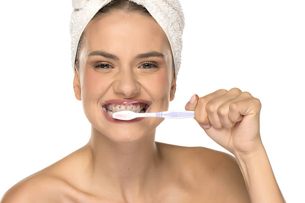 istock Young woman brushing teeth and looking aside, smiling slightly, studio shot on white background. 2233545868