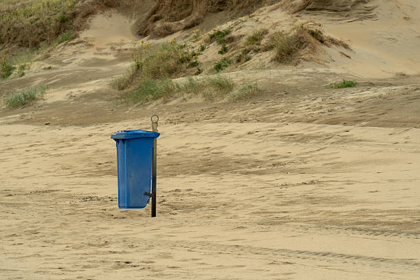 Blue trash can stands on a sandy beach in wassenaar, netherlands, promoting environmental awareness and responsible waste disposal