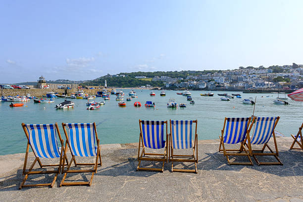 06 AUG 2025 - St. Ives, Cornwall, England, UK - Deck chairs in a row on the harbour side at St. Ives in Cornwall, waiting for holiday makers to rent them on this hot summers day.