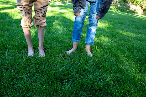 istock Barefoot individuals stand on a lush green lawn in bright sunlight. 2233549207