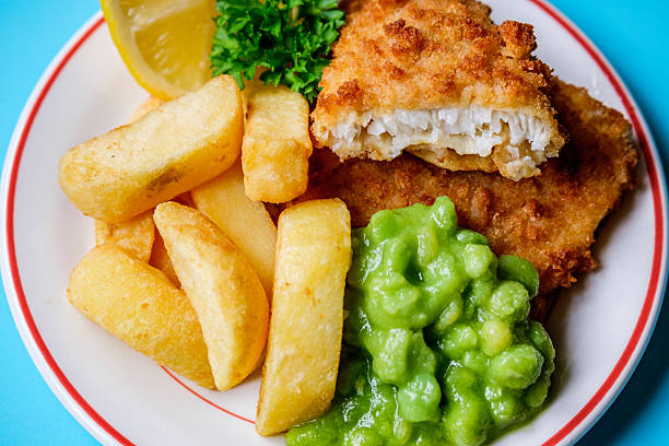 close-up of Baked Cod with Crackers butter toppings served with boiled snow peas and lemon on white plate on white wood table