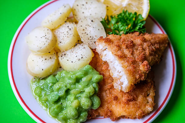 Traditional British Fish and Chips with tartar sauce on plate   and green peas on white wood background.