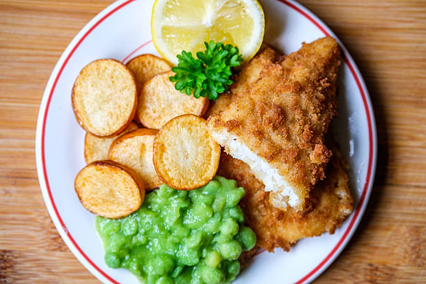 Traditional British Fish and Chips with tartar sauce on plate   and green peas on white wood background.