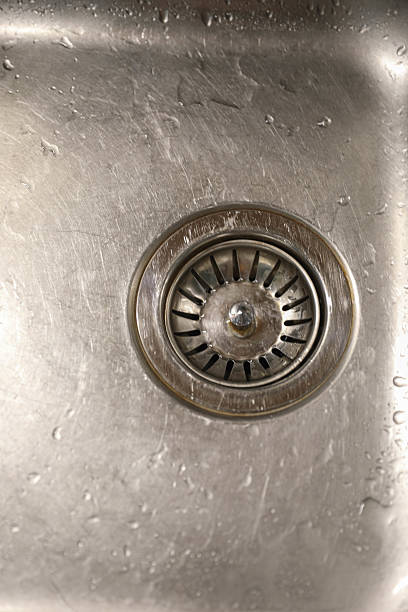 Close-Up Of Stainless Steel Kitchen Sink With Water Drops Around Drain Hole. Concept Represents Hygiene, Plumbing, Sanitation, Domestic Cleaning, And Everyday Household Maintenance.