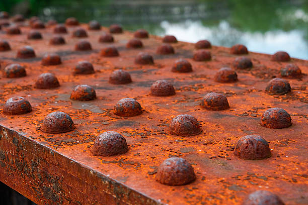 Rusty rivets covering a metal surface near a body of water, indicating deterioration and age