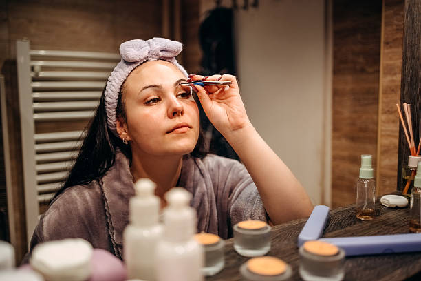 Young female adult standing in front of mirror in the bathroom at home doing her eyebrows