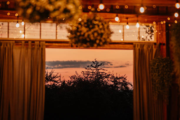 A stunning sunset view framed by an open barn doorway, with hanging lights and draped curtains creating a warm and romantic evening ambiance.
