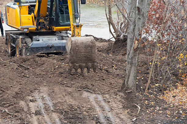 The excavator with its bucket performs the final leveling of the ground before construction begins.