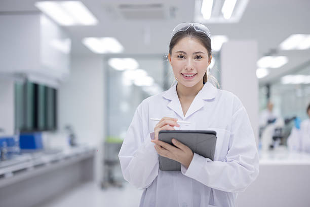 Asian female scientist wearing a lab coat holding a tablet and smiling in a modern laboratory