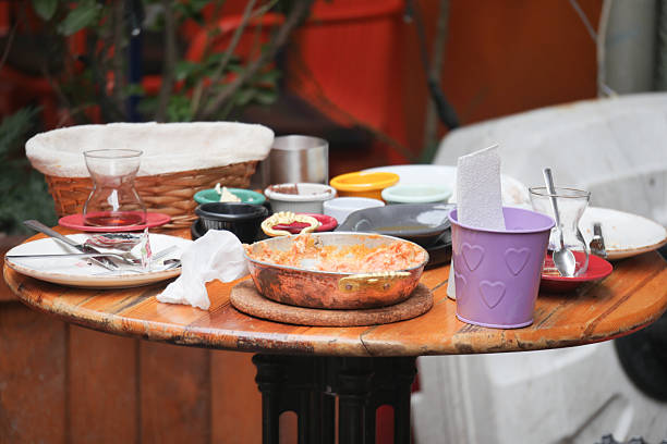Empty dishes and leftover food clutter a round wooden table at a cafe.