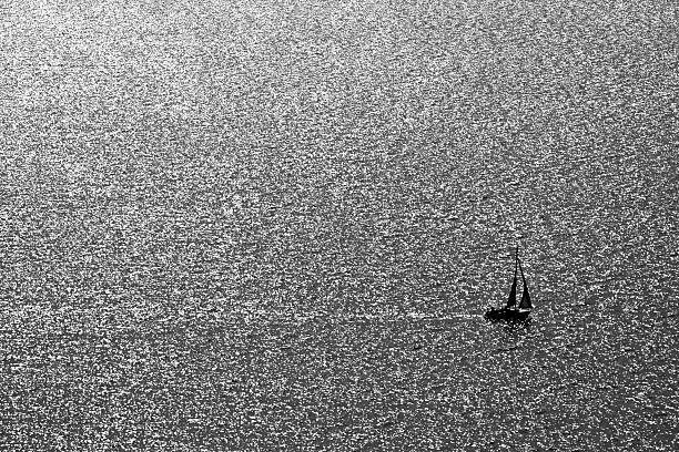 Sailboat silhouetted on shimmering water surface in black and white, Tihany, Lake Balaton, Hungary