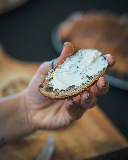 istock Hand holding rustic bread slice topped with creamy cheese spread in a close-up view 2233573459