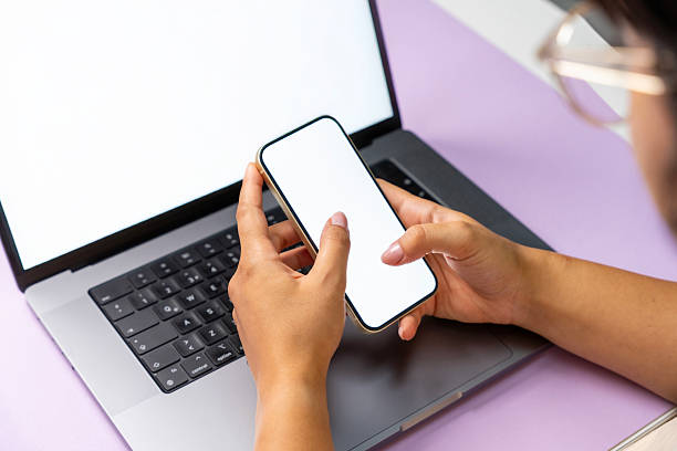 istock Hands Holding Smartphone in Front of Laptop on Modern Desk 2233575522