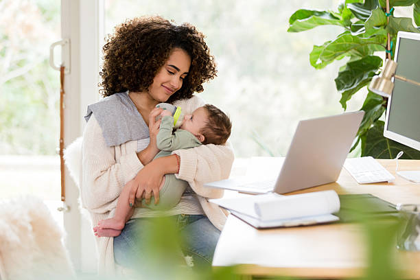 istock Working Mother Feeding Baby, Laptop on Desk 2233586079