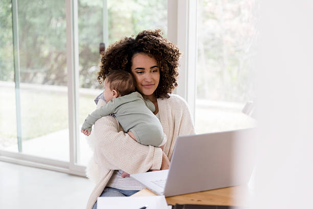 istock Working Mother Holding Baby, Using Laptop, Modern Lifestyle 2233586138